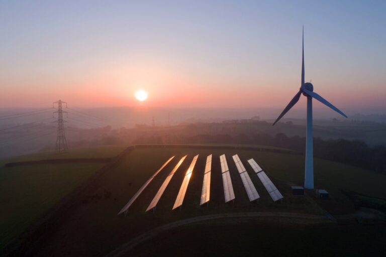 Solar panels and wind turbines in field at sunset